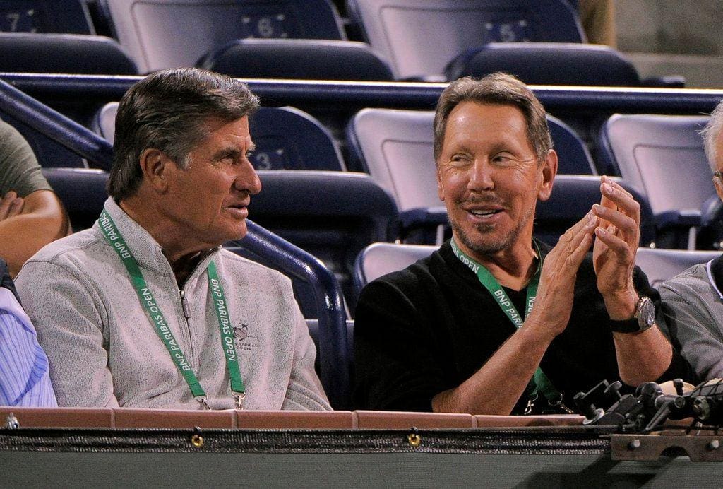 Larry Ellison watching play courtside at the BNP Paribas Open at Indian Wells, wearing tournament credentials, seated in front row of Stadium 1.